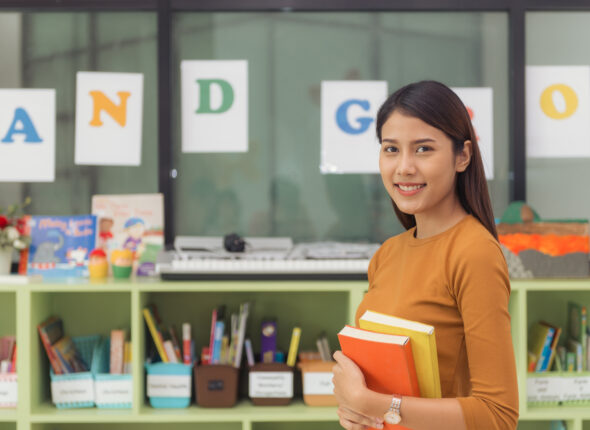 Pretty asian teacher smiling at camera at back of classroom at t
